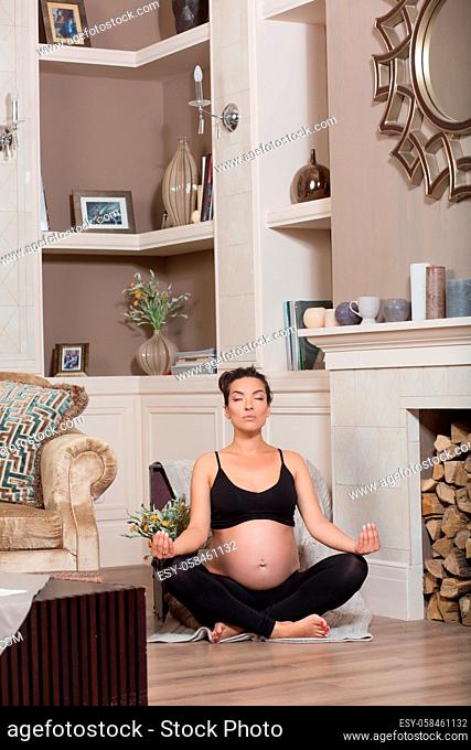 Pregnant lady training for her baby near fireplace log pieces in vintage interior. Brunette lady meditating with her eyes closed