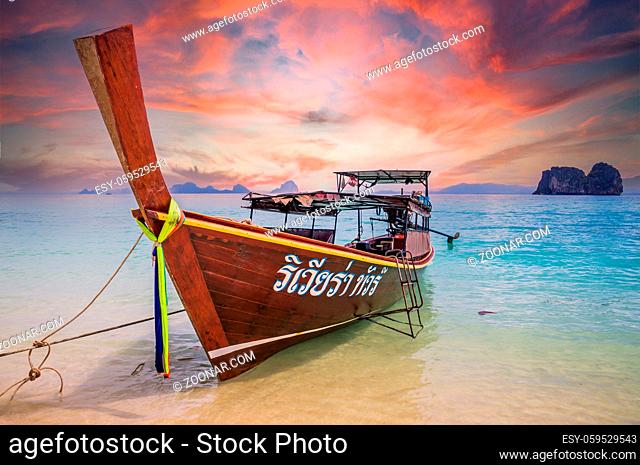 Beautiful sunset sky over longtail boat in crystal clear blue waters waiting for passengers on beautiful white beach in Ko Mok, Thailand