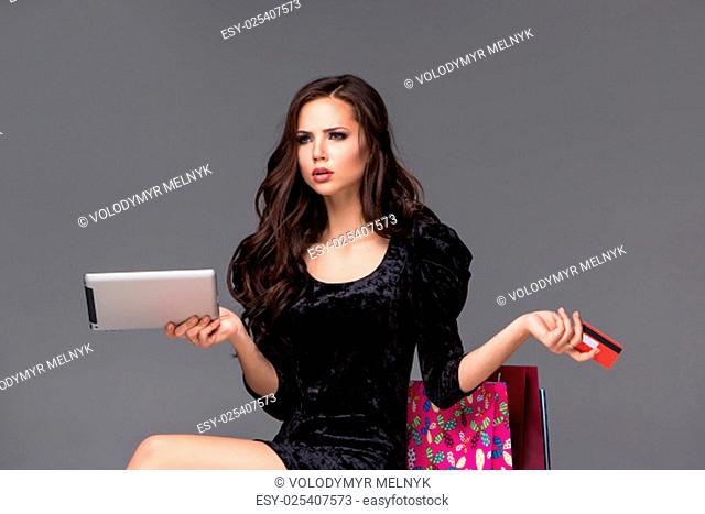 Beautiful young girl paying by credit card for shopping with a laptop and packages against gray background