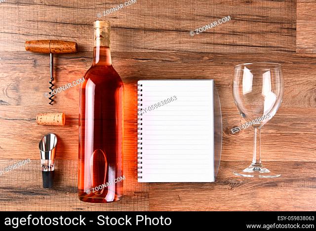 A high angle view of a wine bottle tasting notes notebook, cork screw, and wine glass on a wood table
