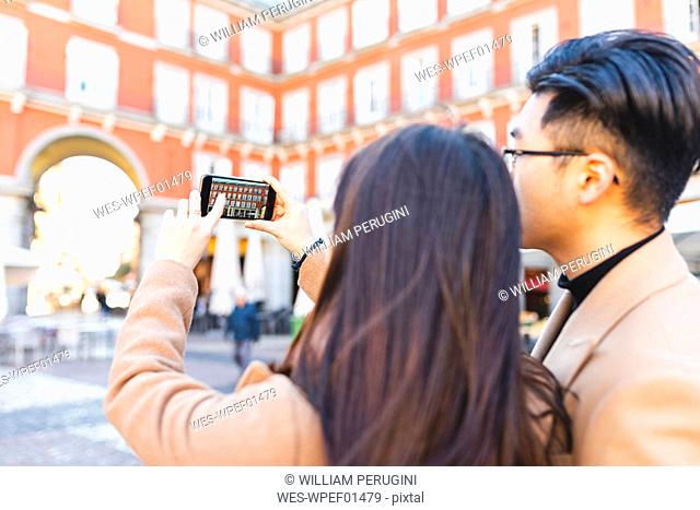 Spain, Madrid, young couple taking a smartphone picture in the city