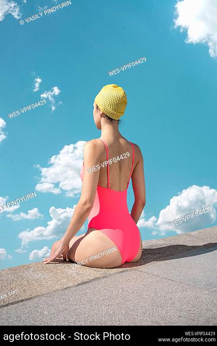 Woman with swimming cap and swimsuit sitting at edge