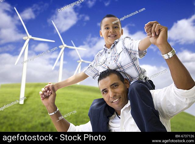 Happy hispanic father and son with wind turbine farm over blue sky
