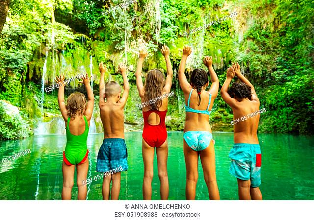 Happy children jumping into the mountain's lake, amazing nature, great greenery surrounded the lake, holidays in the beautiful natural place, summer camp