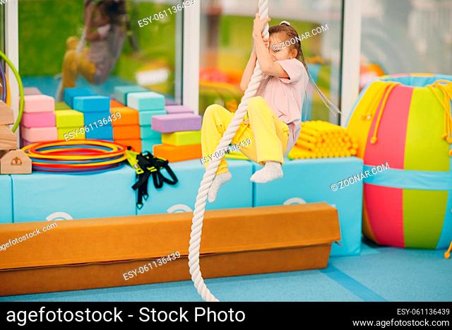 Kids doing exercises climbing tightrope in gym at kindergarten or elementary school. Children sport and fitness concept