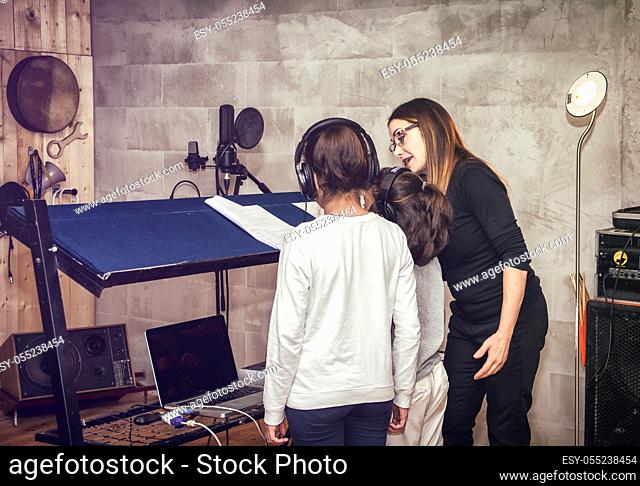 Rear view of two unrecognizable children in headphones with female acting or singing teacher in recording studio