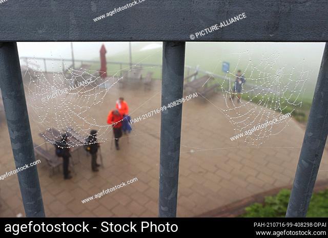 16 July 2021, Bavaria, Oberstdorf: Hikers stand on the 1967 high summit station of the Fellhornbahn behind spider webs covered with water drops in the fog