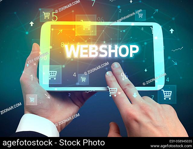 Close-up of a hand holding tablet with WEBSHOP inscription, online shopping concept
