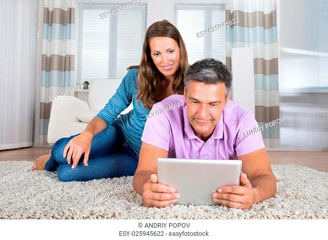 Matured Smiling Couple Looking At Digital Tablet In Living Room