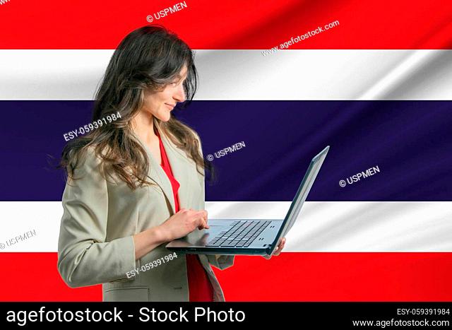 Freelance in Thailand. Beautiful young woman freelancer uses laptop computer against the background of the flag of Thailand