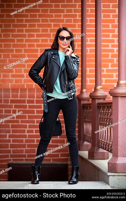 Young fashion woman with handbag walking in city street Stylish female model in black leather jacket outdoor
