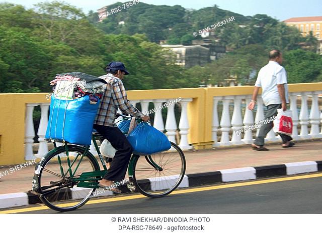 Blue luggage being transported on a bicycle over Old Pato bridge ;  Yellow bridge on the Mandovi River ;  Mahatma Gandhi Road ;  Panjim ;  Goa  ; India