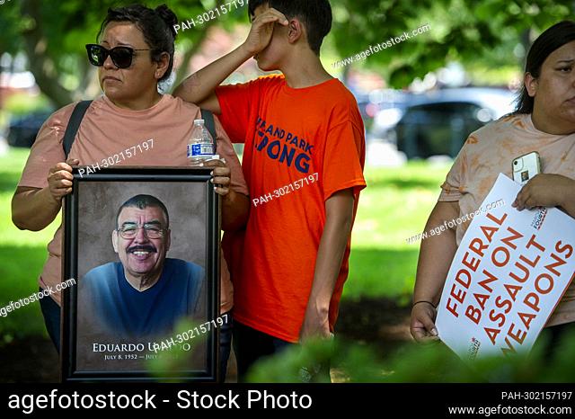 Nubia Hogan, left and her son Brian Hogan, 13, stand in the shade of a tree, with a photo of her father Eduardo Uvaldo, who was killed in the recent mass...