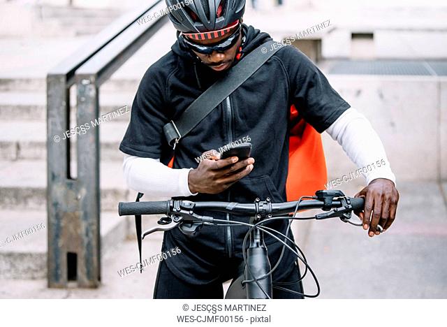 Stylish young man with bicycle, smartphone and messenger bag in the city