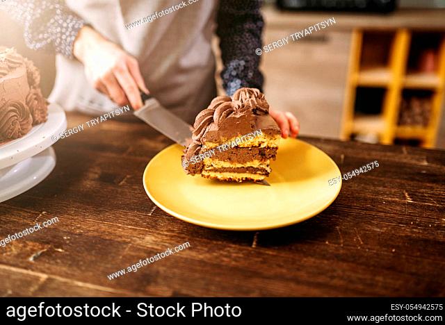 Female hands holds piece of chocolate cake on the blade, culinary masterpiece. Kitchen on background. Homemade sweet dessert