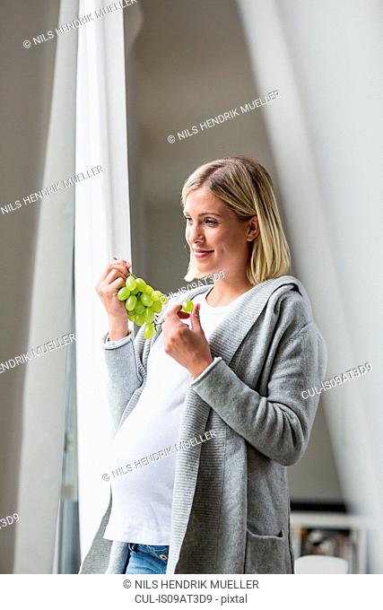 Full term pregnancy young woman eating grapes
