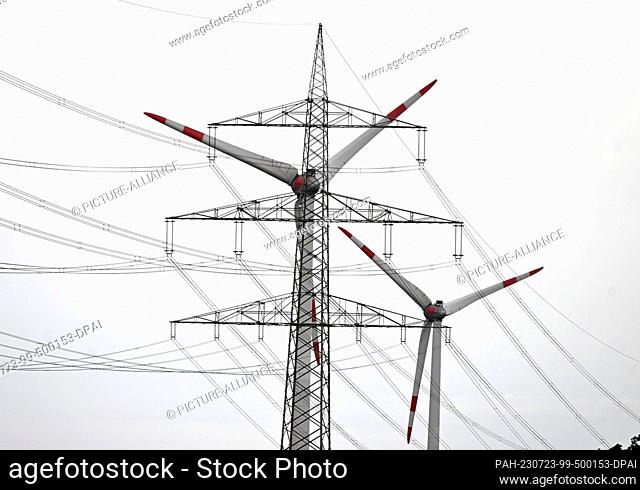 23 July 2023, North Rhine-Westphalia, Inden: A wind turbine turns next to an overhead power line in the Rhenish lignite mining area