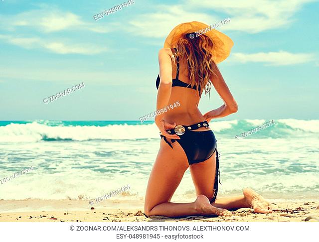 Sexy blond woman wearing swimsuit posing on the beach near the sea