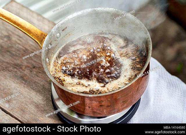 working steps with fennel and fennel seeds for the preparation of fennel syrup, view into a copper saucepan with a boiling solution of fennel seeds and cane...