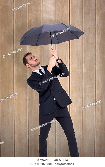 Composite image of businessman standing under black umbrella