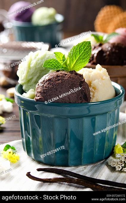 Three scoops of Vanilla pistachio and chocolate icecream balls in clay bowls on wooden kitchen table