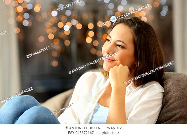 Candid woman dreaming sitting on a couch in the living room at home with little lights in the background