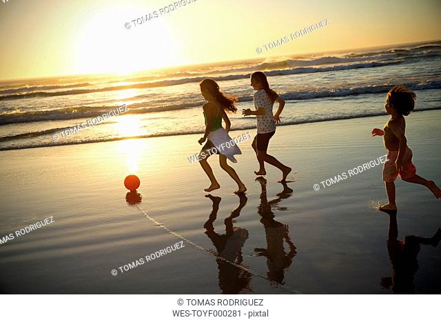 Three children playing with ball on the beach at sunset