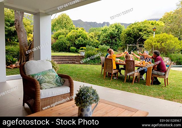 Caucasian three generation family sitting at table making a toast during meal in garden