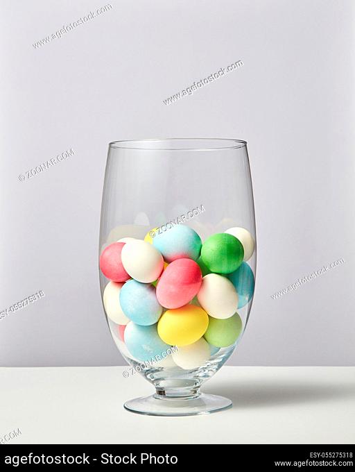 Multi-colored painted eggs in a glass vase on a gray background with space for text. Easter concept