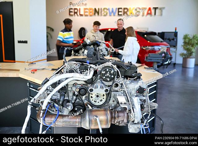 04 September 2023, Saxony, Leipzig: Instructor Lars Bergemann (2nd from right) explains a 4-cylinder boxer engine to students in the Porsche experience workshop