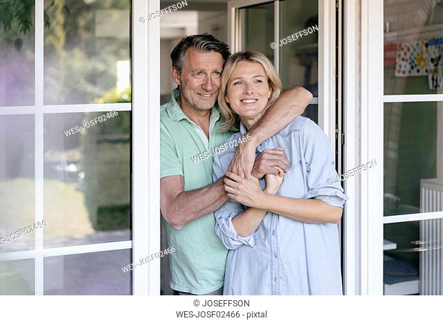 Happy mature couple hugging at French window