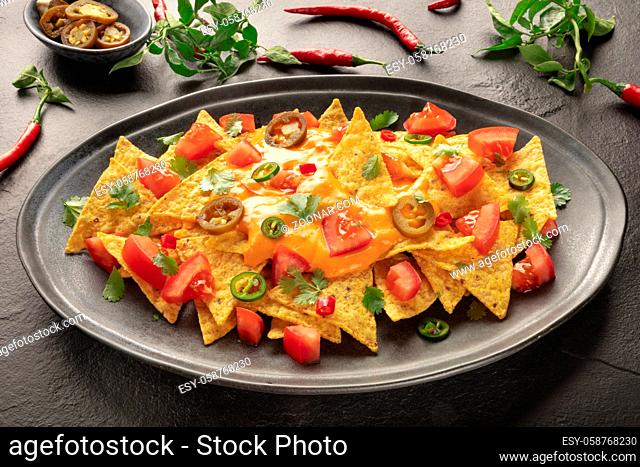 Mexican nachos with a cheese sauce, chili and jalapeno peppers, tomatoes, and cilantro on a black background