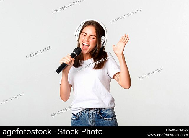Carefree smiling girl playing karaoke, singing in microphone with headphones