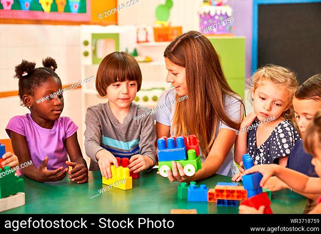 Erzieherin und Kinder im internationalen Kindergarten spielen zusammen mit bunten Bausteinen