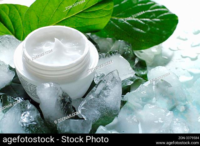 A jar of a cosmetic cream with fresh green leaves and pieces of ice. Beauty concept.