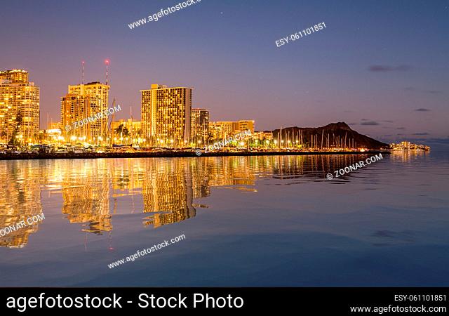 Panorama of the nightime skyline of Honolulu and Waikiki from Ala Moana park after the sun sets with artificial water reflection