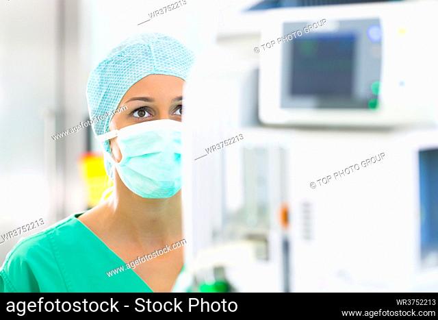 Hospital operating room - Young female doctor or surgeon in a sterile operating theater of clinic controlling data a heart monitor