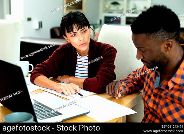 Multiracial young couple with laptop discussing household expense budget over bill at home