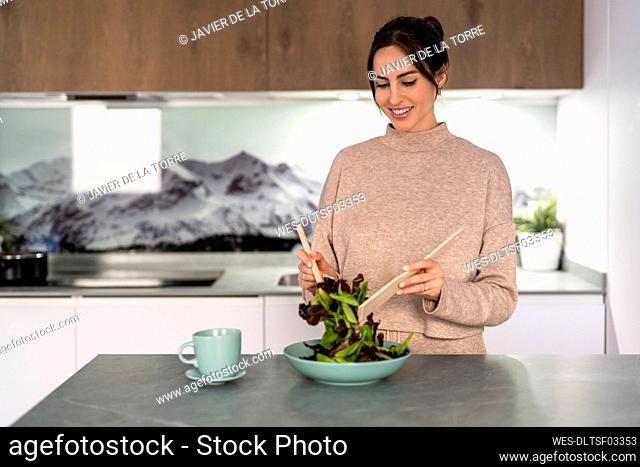 Smiling young woman preparing salad at home