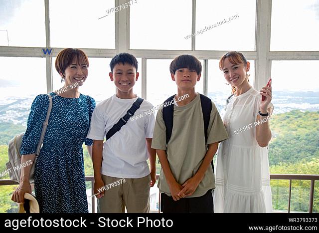 Four Japanese people, two boys and two mature women on a day out, posing for a photograph, side by side, on a viewing platform