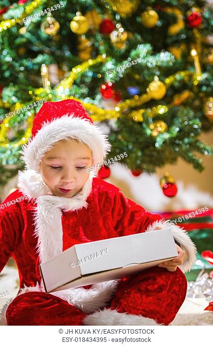 Surprised boy opens a Christmas gift, Christmas tree and gifts on background