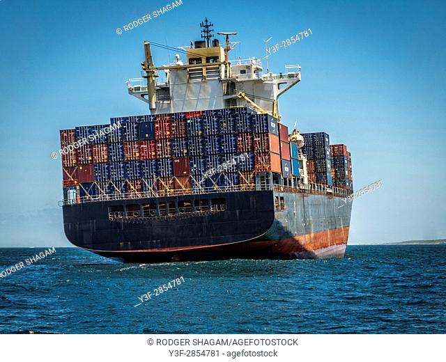 A container ship rolls gently on a flat sea while at anchor
