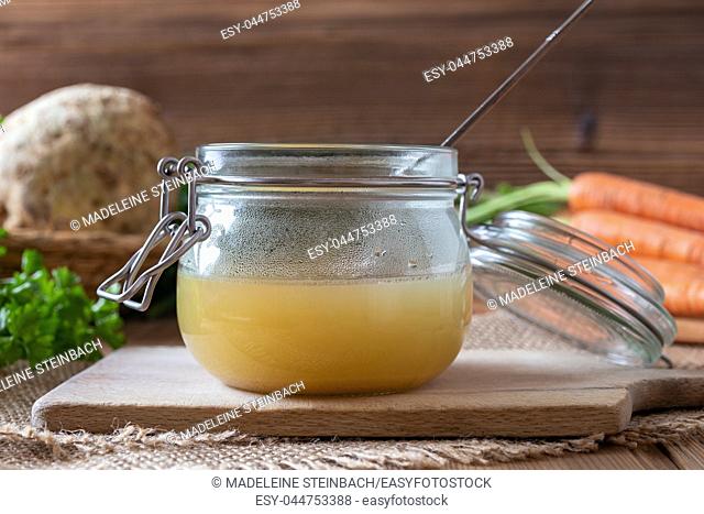 Chicken bone broth in a glass jar and fresh vegetables on a table