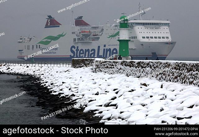 06 December 2023, Mecklenburg-Western Pomerania, Warnemünde: The pier of the Baltic seaside resort is covered in snow while a Scandinavian ferry from Stena Line...