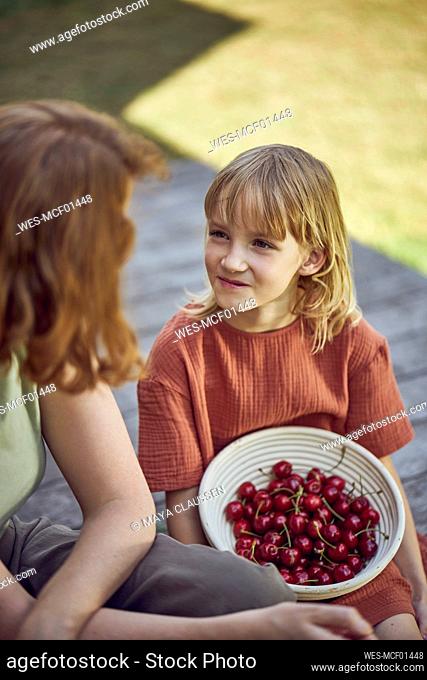 Mother sitting with eating cherries while sitting in yard