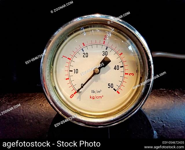 a round shiny pressure gauge with numbers marked in psi and metric on the meter dial on industrial machinery