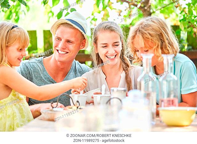 Glückliche Familie und Kinder sitzen entspannt beim Kaffee am Gartentisch