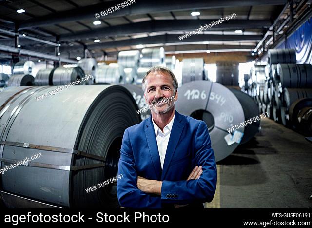 Smiling businessman with arms crossed standing at warehouse