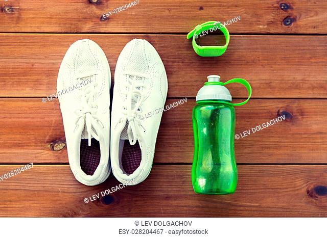 sport, fitness, healthy lifestyle and objects concept - close up of sneakers, bracelet and water bottle on wooden floor