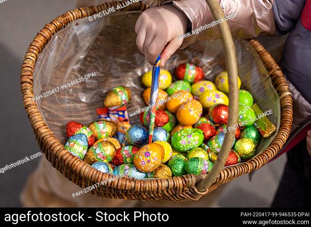 17 April 2022, Thuringia, Erfurt: A child takes chocolate from a basket of Easter eggs distributed by a person in an Easter bunny costume in Ega Park
